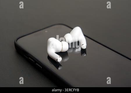 White earbuds rest on black smartphone screen. Minimalist setup, sleek design, clean reflection. Modern tech aesthetic, contemporary lifestyle. Simple Stock Photo
