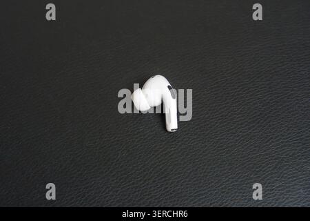 Single white earbud rests on dark textured surface. Minimalist composition highlights sleek design. Clean lines emphasize modern technology aesthetic. Stock Photo