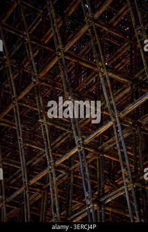Dark diagonal bamboo lattice ceiling structure with intricate crossing pattern, moody low-key texture background. Stock Photo