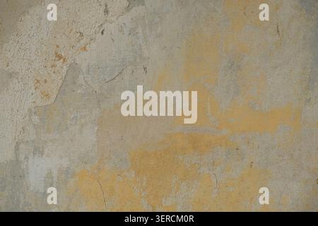 Close-up of a weathered plastered wall with peeling and flaking paint in shades of beige, grey and ochre yellow, showing signs of age and decay Stock Photo