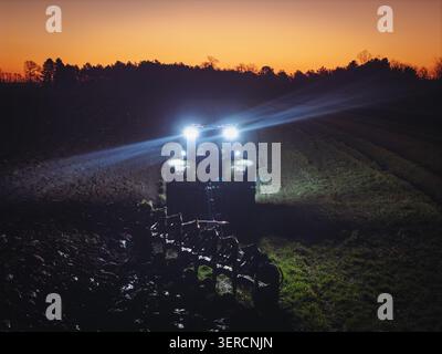 close up Tractor Plowing Field at night with headlights Stock Photo