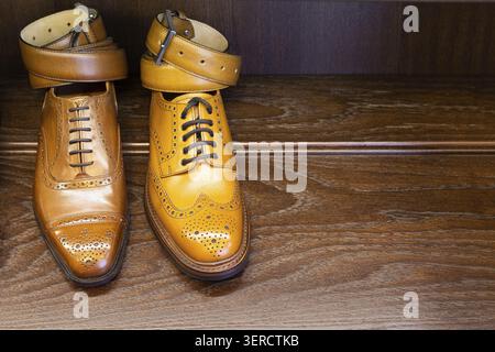 Brown and tan full grain leather shoes with belts on wooden display in men shoes boutique store Stock Photo