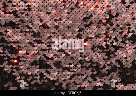 Sequin fabric background. Close-up shot of glittery black sequins texture reflecting red light Stock Photo