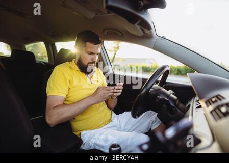 Young bearded man using smartphone while sitting in car driver seat Stock Photo