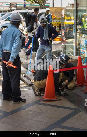 Nara, Japan April 20, 2026 workers performing maintenance on street drainage with tools and safety cones on sidewalk Stock Photo