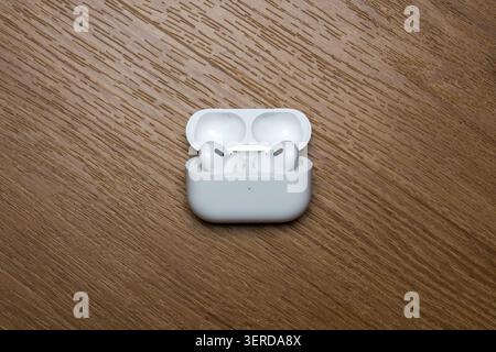 White earbuds rest in open case. Case sits on wooden surface. Clean, minimalist design. Simple background emphasizes product. Ideal for tech or lifest Stock Photo