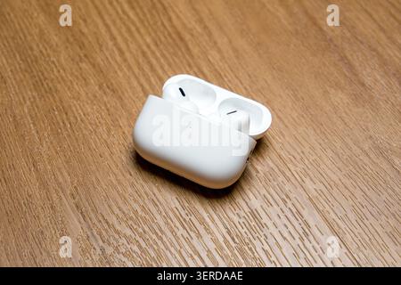 White earbuds rest in open charging case. Case sits on light wood surface. Minimalist, clean design visible. Soft lighting highlights product details. Stock Photo