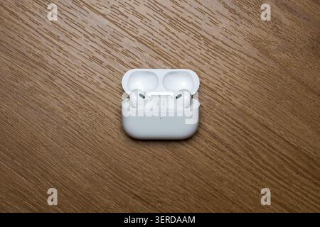 White wireless earbuds rest open in their charging case. Case sits on a warm-toned wooden surface. Minimalist design highlights clean lines and smooth Stock Photo
