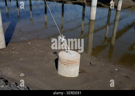 A close-up view of the engineering details of a floating photovoltaic power station. On the concrete cylindrical anchor block by the shore, rusty meta Stock Photo