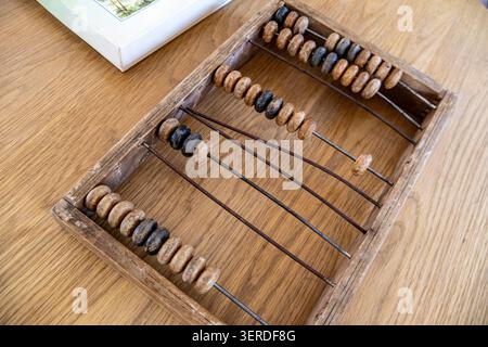 A close-up horizontal shot of an antique traditional wooden abacus frame with rows of worn dark counting beads, resting on a natural light grain timbe Stock Photo
