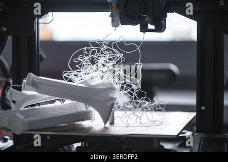 Fdm 3d printer failing during the additive manufacturing process, creating a tangled mess of extruded white plastic filament on the print bed, emphasi Stock Photo