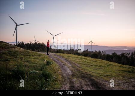 Man standing on a dirt road, looking at wind turbines generating clean power Stock Photo
