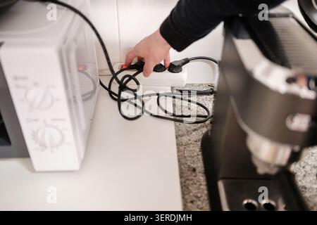 Person powering off a multi-socket adapter for energy conservation in a kitchen Stock Photo