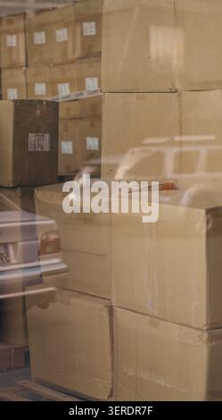 Cardboard boxes stacked inside warehouse behind reflection window close up. Stock Photo