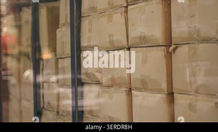 Cardboard boxes stacked inside distribution warehouse behind glass window close up. Stock Photo