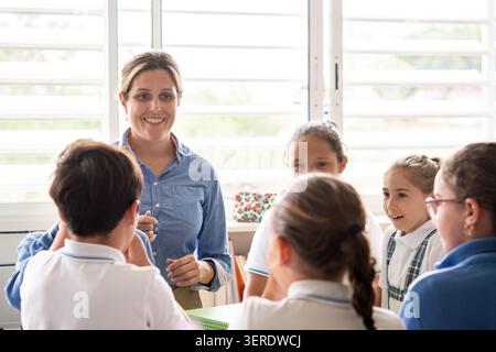 Primary school teacher engaging a group of students in a collaborative classroom discussion. Stock Photo