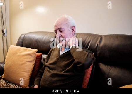 Senior man suffering from aching neck, touching his painful area at home Stock Photo