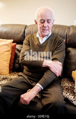 Senior man suffering from joint pain in his elbow while resting at home Stock Photo
