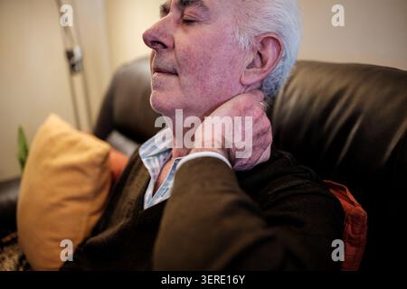 Senior man sitting with eyes closed, rubbing his sore neck Stock Photo