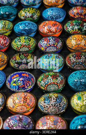 A close-up vertical shot displays an abundant collection of vibrant, hand-painted ceramic bowls arranged neatly on a dark surface. Each bowl features Stock Photo