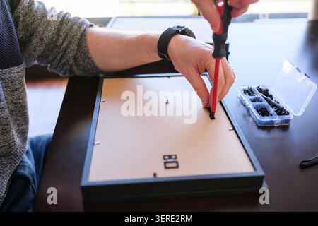 Person's hands assembling a picture frame using a screwdriver and small clips Stock Photo