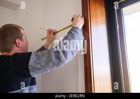 Man measuring dimensions of a wall near a window with a tape measure and pencil Stock Photo