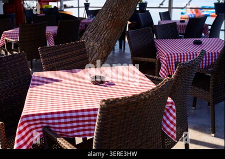 Wooden tables covered with red and white gingham checkered tablecloths on an outdoor cafe terrace. Stock Photo