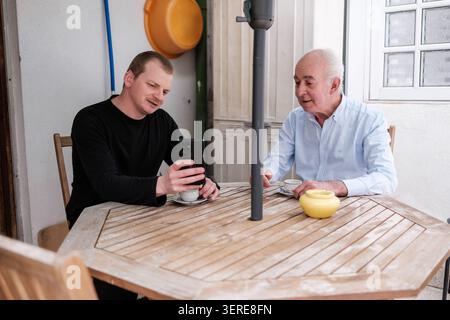 Younger man showing smartphone to an elderly man while having coffee together Stock Photo