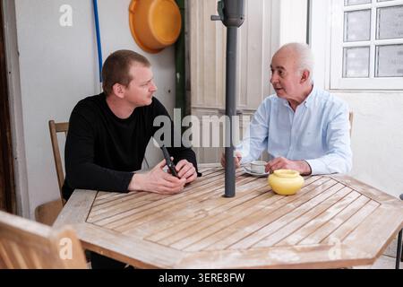 Two men of different generations having a conversation while sitting at a wooden table Stock Photo