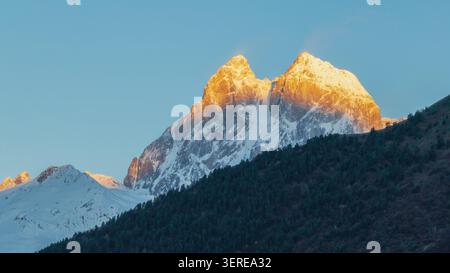 Panoramic view of the sunrise at Ushba mountain. Beautiful shinning mountain peak range. Georgia. Stock Photo