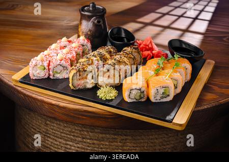 Fresh sushi is arranged on a wooden platter. Different types of sushi roll are visible, along with slices of pickled ginger and wasabi. Soy sauce is in small bowls nearby for dipping. Stock Photo