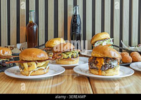 On a large, striped metal tray, several vacuum-packed beef burgers with melted cheese are lined up, surrounded by mounds of crispy fries, a bowl of st Stock Photo