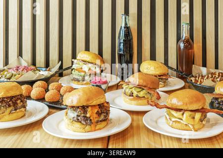 On a stainless steel surface, multiple perfectly formed Angus beef burgers are arranged in two irregular rows, next to a kitchen thermometer, a jar of Stock Photo