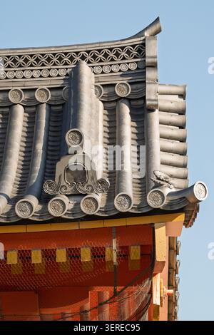 Traditional grey clay tile roof ridge with curved end caps on an orange temple building, Kyoto, Japan Stock Photo