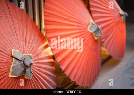 Three traditional orange oil-paper parasol umbrellas unfolded and resting outdoors on the ground, Kyoto, Japan Stock Photo
