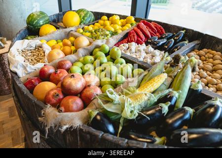 Vibrant assortment of seasonal produce including pomegranates, apples, corn, eggplants, peppers, nuts arranged in wooden barrels. Natural lighting highlights textures colors Stock Photo