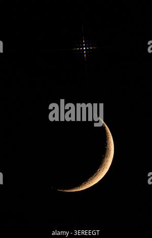 Crescent moon illuminating craters on dark night sky with a starburst star Venus Stock Photo
