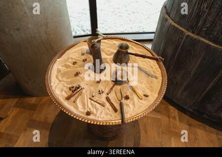 Copper cezve, grinder, and spices arranged on warm sand in a copper tray, evoking a cozy cafe atmosphere with rustic wooden textures and soft natural lighting Stock Photo