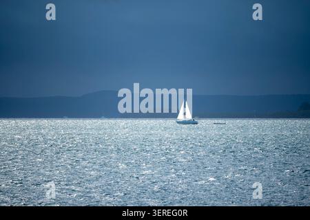 Lone Sailboat on Shimmering Blue Water Under Dramatic Sky Stock Photo