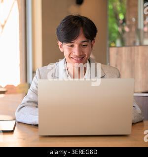 Authentic close up lifestyle portrait of a young non-binary Thai Isan professional or student smiling while looking down at a computer screen. Focused Stock Photo