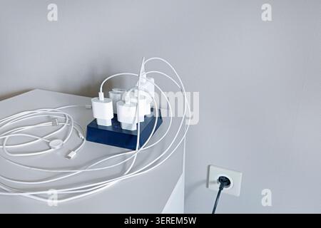 Outdated messy charging station with multiple tangled wired power adapters on desk. Daily technology problem showing excessive cable clutter before Stock Photo