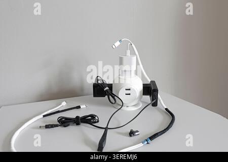 White desktop power cube hub with black adapters and multiple usb charging cables. Tech clutter mess problem on table inside modern minimalist studio Stock Photo