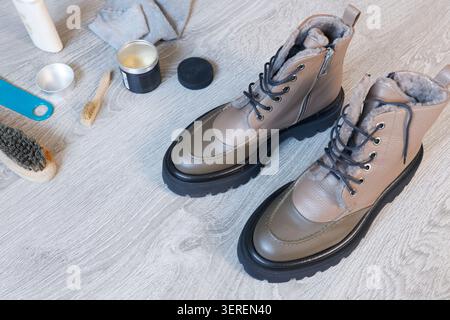 Premium winter leather boots care kit with polish cream wax and wooden brushes on floor. Footwear maintenance routine for high quality material Stock Photo
