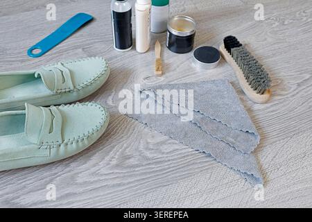 Mint green suede loafers care kit with wooden brushes wax cream and cloth on floor. Elegant summer footwear maintenance routine for premium leather Stock Photo