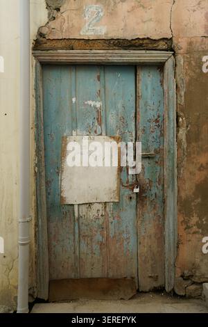 A close-up view of an aged and weathered wooden door, painted in a faded teal color with extensive peeling paint and visible raw wood. Above the door Stock Photo