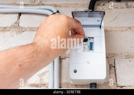 Hand flipping a circuit breaker switch in an electrical distribution box. Electrician or homeowner operating a power switch in a residential fuse box. Stock Photo