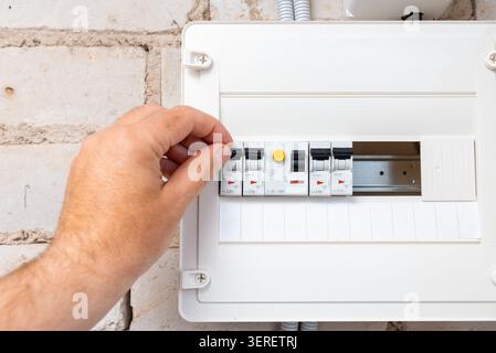 Close-up of a hand operating a modular circuit breaker in an electrical panel. Electrician flipping a circuit breaker switch in a home distribution bo Stock Photo