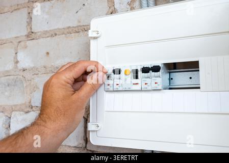 Close-up of a hand operating a modular circuit breaker in an electrical panel. Electrician flipping a circuit breaker switch in a home distribution bo Stock Photo