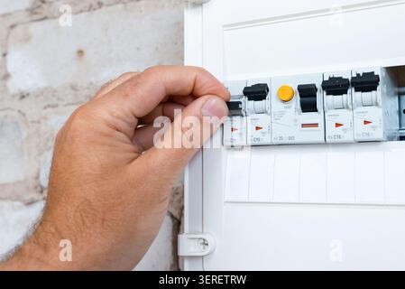 Close-up of a hand operating a modular circuit breaker in an electrical panel. Electrician flipping a circuit breaker switch in a home distribution bo Stock Photo