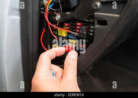 Mechanic hand removing a car fuse from the vehicle fuse box. Close-up of replacing a burnt automotive electrical fuse. Stock Photo